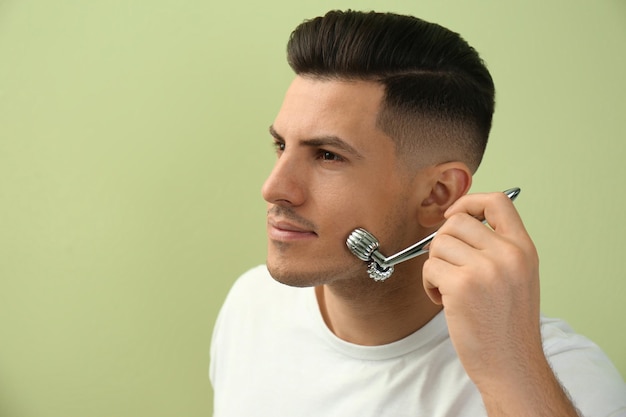 Man using metal facial roller on green background