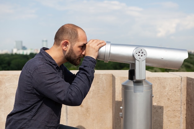 Man using panoramic binoculars telescope looking at metropolitan city