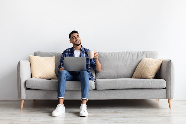 Man using pc sitting on the couch drinking coffee