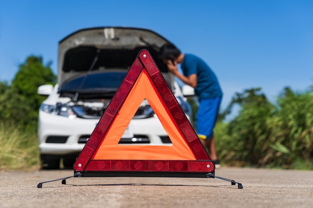 A man using a phone while having a problem car and a red triangle warning sign on the road