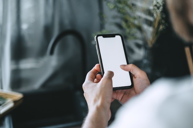 Man using smartphone with a white blank screen in the kitchen.