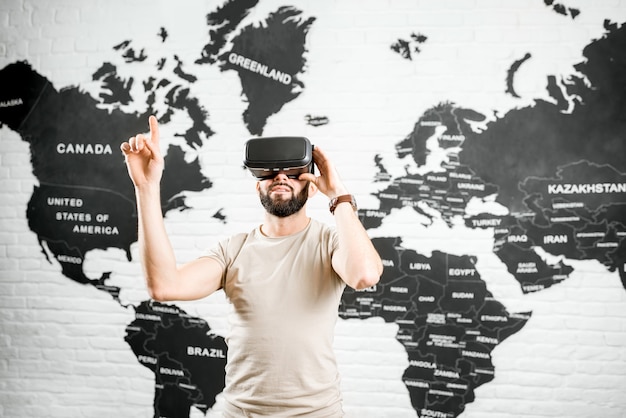 Man using virtual reality glasses sitting indoors with world map on the background