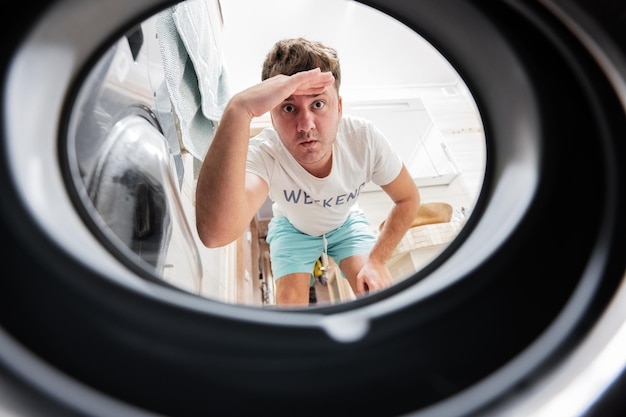 Man view from washing machine inside Male does laundry daily routine Hand over forehead looking far away watching or searching