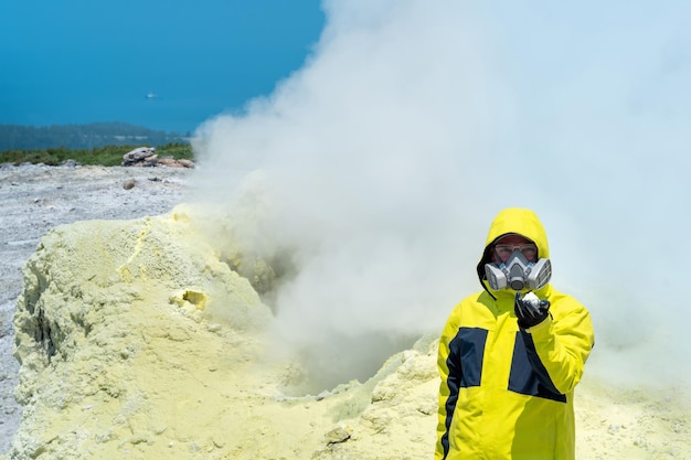 Man volcano scientist on the slope of a volcano among the vapors of a fumarole with sample of a mineral in his hand