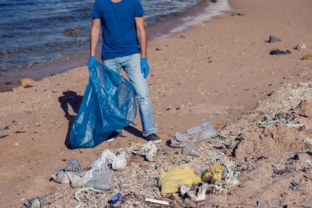 Man volunteer with big bag for trash collecting garbage on beach. Environmental pollution concept