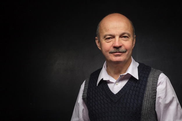 Man in a waistcoat looking confidently forward Lecturer stands in black chalk wall