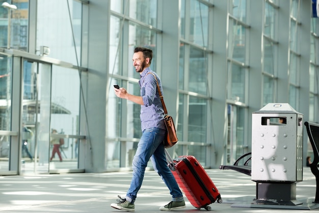 Photo man walking at airport with suitcase and mobile phone