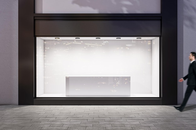 Man walking by evening empty shop window with podium inside for your product presentation on glowing white background in modern building area outdoors mock up