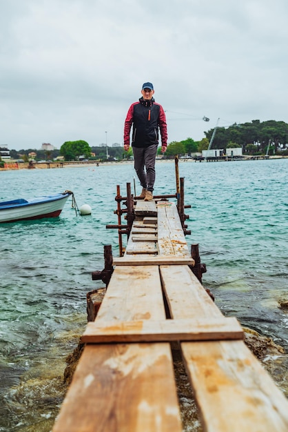 man walking by small wooden pier overcast weather stormed sea on background