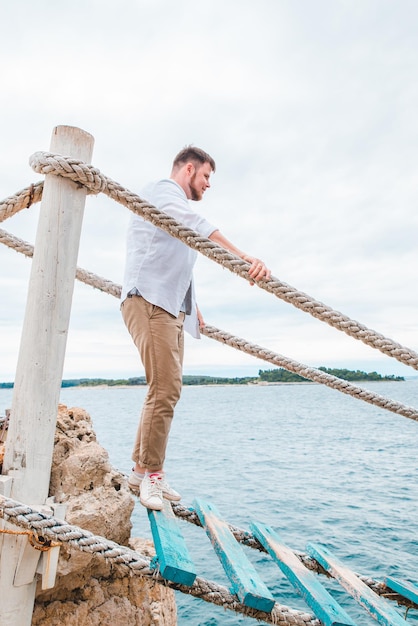 Man walking by tourist suspension bridge crossing sea bay