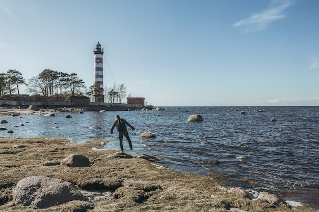 Man walking on the stony sea coast next to the lighthouse.