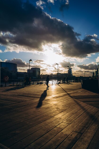 Photo a man walks across a boardwalk with the sun setting behind him