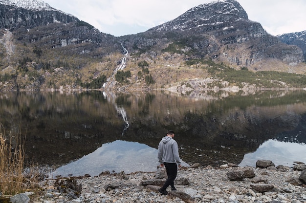 Man walks beside fjord with mountain reflection