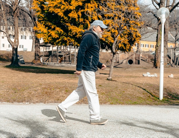 A man walks down a sidewalk in front of a tree with a house in the background.