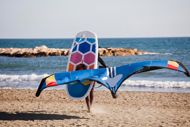 Man walks with equipment to practice wing foil on the beach