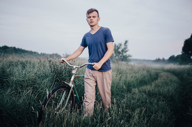 man walks with a green retro bicycle on a field road and grass in summer