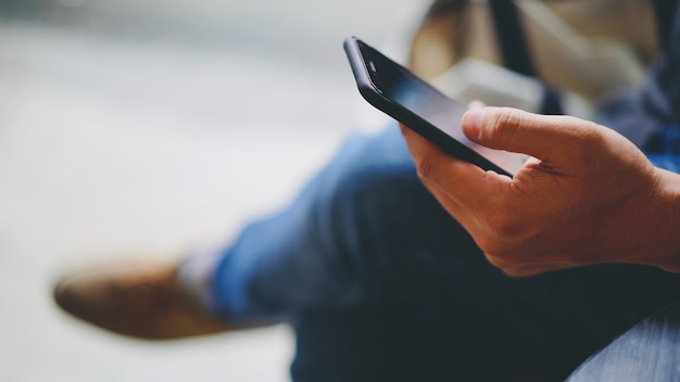 Man waring jeans using smartphone with left hand, copy space on left