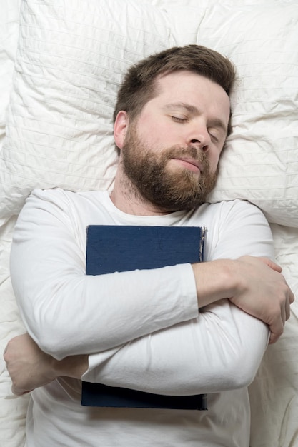 Man was reading while lying in bed and fell asleep hugging a book Top view