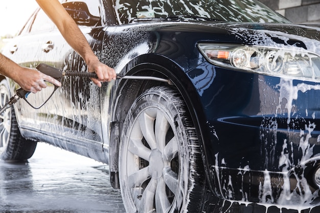 The man washes the foam out of the car with the pressure of water