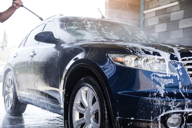 The man washes the foam out of the car with the pressure of water