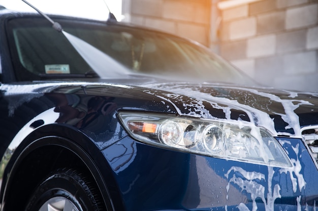 The man washes the foam out of the car with the pressure of water