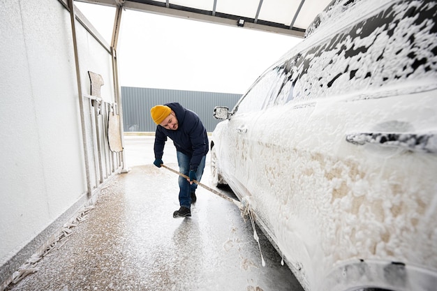 Man washing american SUV car with mop at a self service wash in cold weather