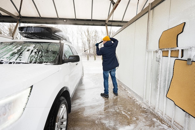 Man washing high pressure water american SUV car with roof rack at self service wash in cold weather