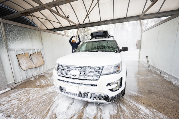 Man washing high pressure water american SUV car with roof rack at self service wash in cold weather