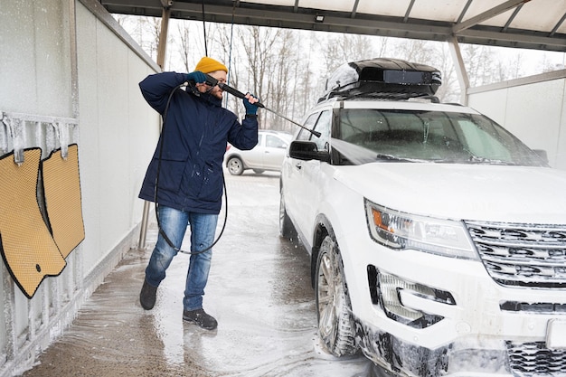 Man washing high pressure water american SUV car with roof rack at self service wash in cold weather