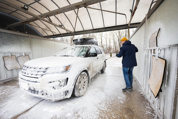 Man washing high pressure water american SUV car with roof rack at self service wash in cold weather