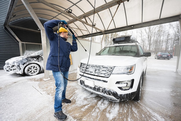 Man washing high pressure water american SUV car with roof rack at self service wash in cold weather