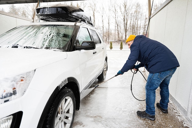 Man washing high pressure water american SUV car with roof rack at self service wash in cold weather