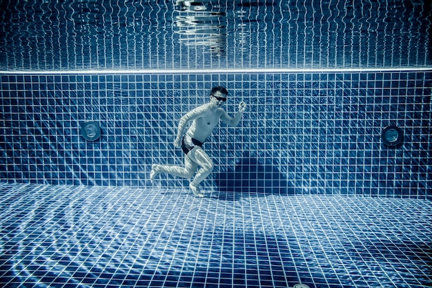 Man under water runs along the bottom of a swimming pool