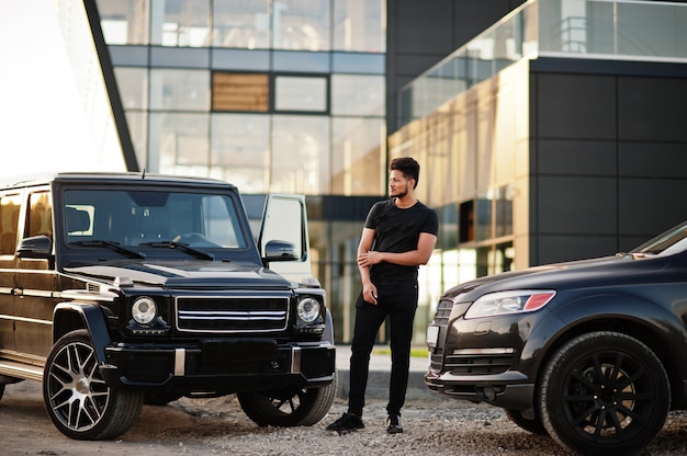 Man wearing all black posing near suv cars