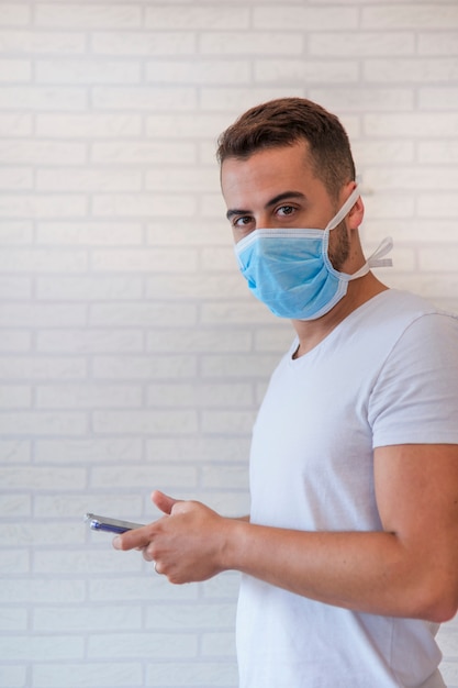 Man wearing an anti virus protection mask to prevent others from getting coronavirus COVID-19 and SARS cov 2, while communicating with loved ones with his smartphone from home.