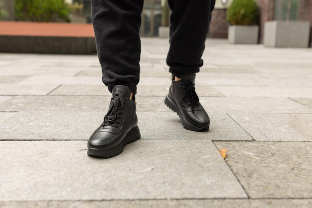 A man wearing black leather boots stands on a sidewalk.