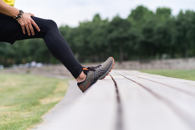 Man wearing black leggings touching sports shoe toe cap leaning on bench and doing exercises