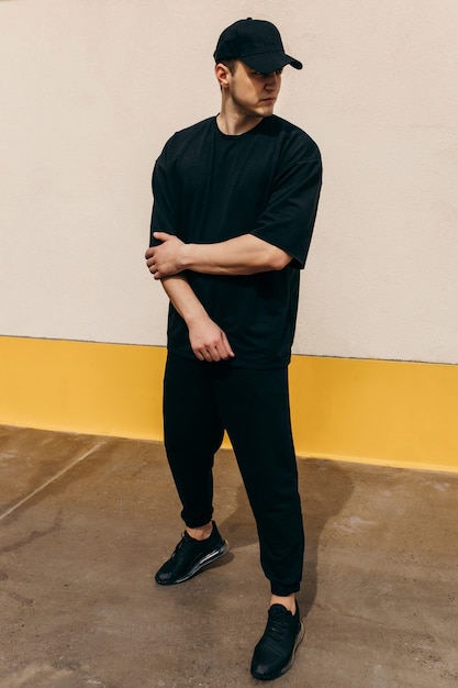 Man wearing black tshirt and a black baseball cap with on an outdoors wall background