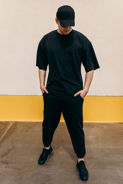 Man wearing black tshirt and a black baseball cap with on an outdoors wall background