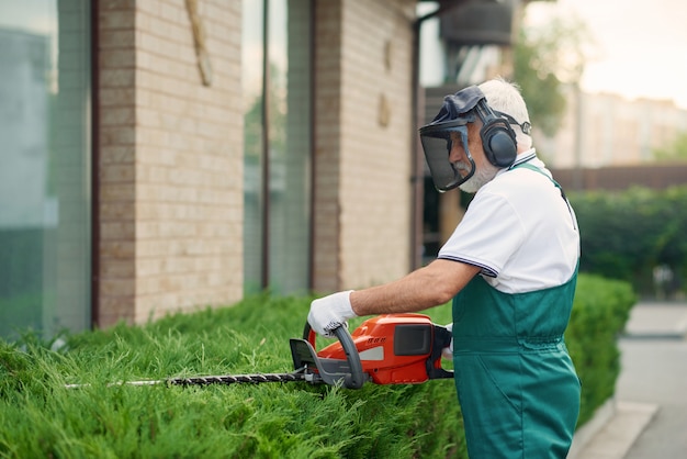 Man wearing ear and face defenders cutting bushes.