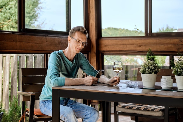 Man wearing glasses using phone looking at smartphone screen and holding glass of wine