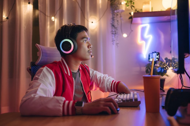 a man wearing headphones sits at a desk with a neon light in the background