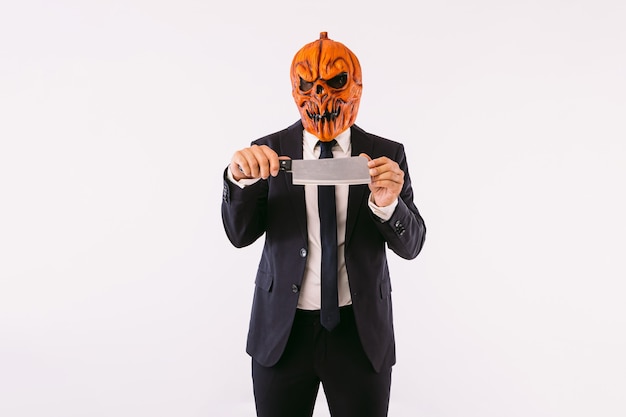 Man wearing jacket suit, blue tie and Jack-o-lantern pumpkin mask, holding a meat cleaver. Halloween and carnival celebration concept.