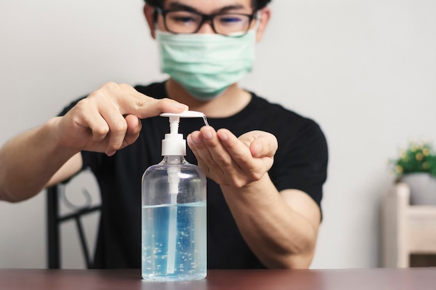 Man wearing a mask cleaning his hands with alcohol gel at home, New normal.