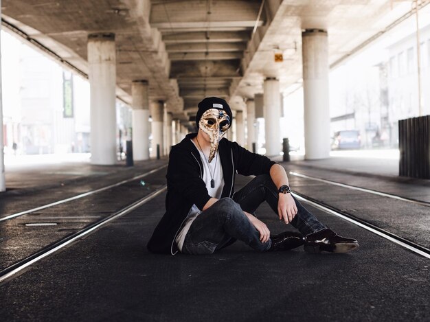 Man wearing mask sitting below elevated road