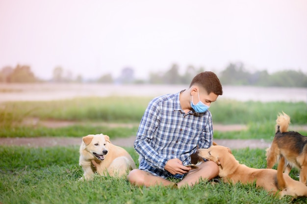 A man wearing a mask, sitting playing with a dog on the lawn. a man stay for home playing with the dog.