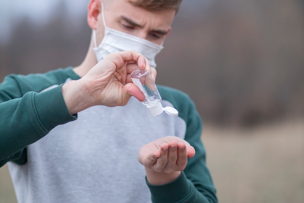 man wearing medical mask using sanitizer