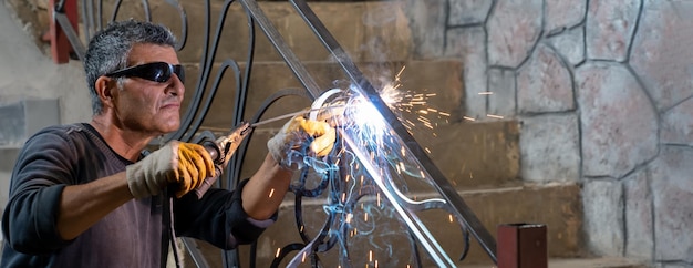 Man wearing protective glasses welds metal with welding machine in private house sparks welding fly