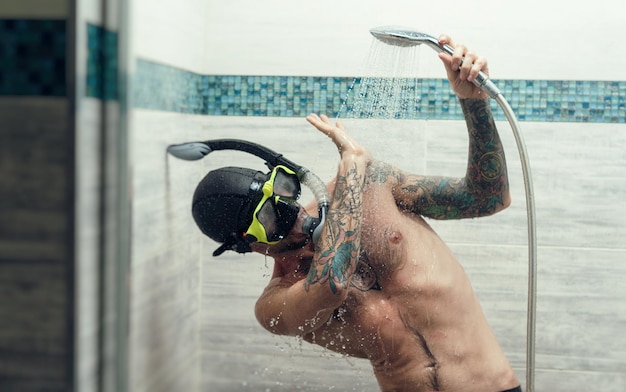 A man wearing a scuba mask in the shower is doused with water