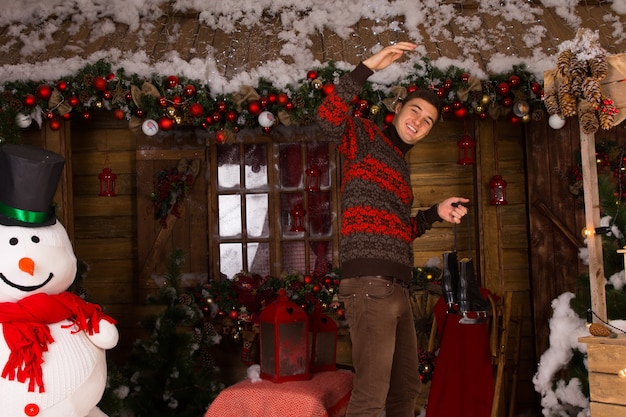 Man Wearing Sweater and Holding Skates in front of Log Cabin in Winter